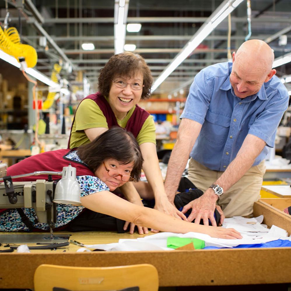 Tom, Lisa and Fong using their hands to block the camera from seeing a large piece of paper with a drawing of a new design on it..