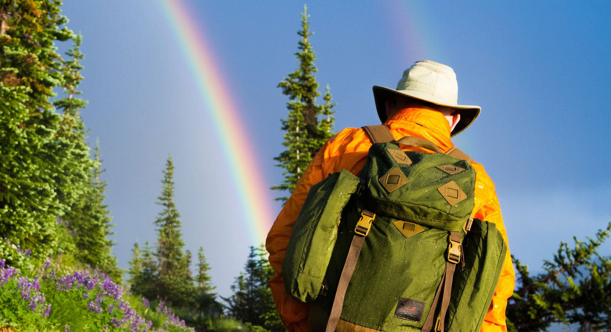 Person carrying an Olive Guide's Pack on a hike; there's a double rainbow in the background!