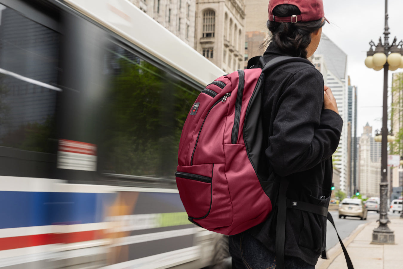 A person wearing a Synapse 25 in Raspberry standing beside a bus.