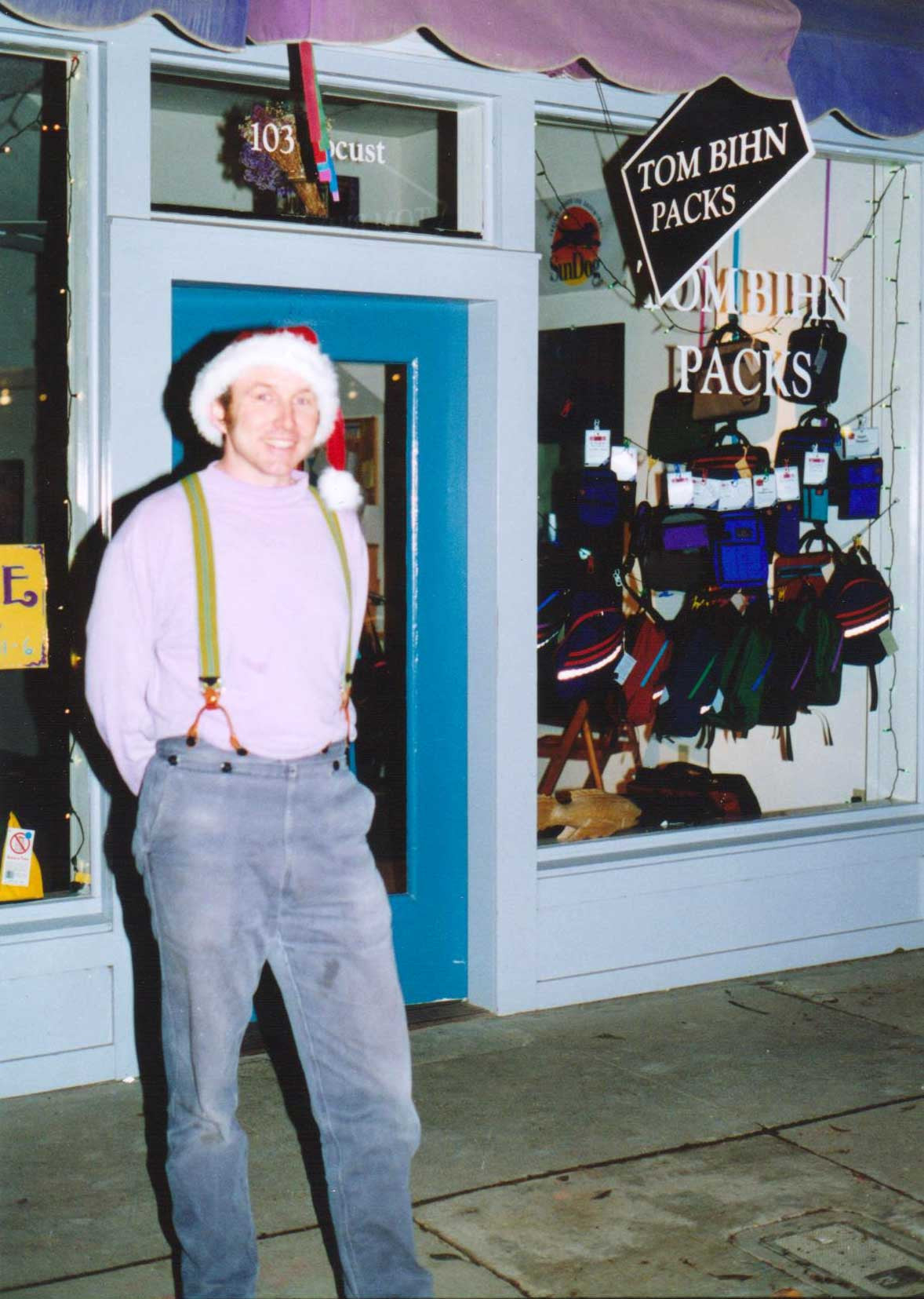 Tom wearing a santa hat and suspenders, standing outside his Santa Cruz shop in 1996.