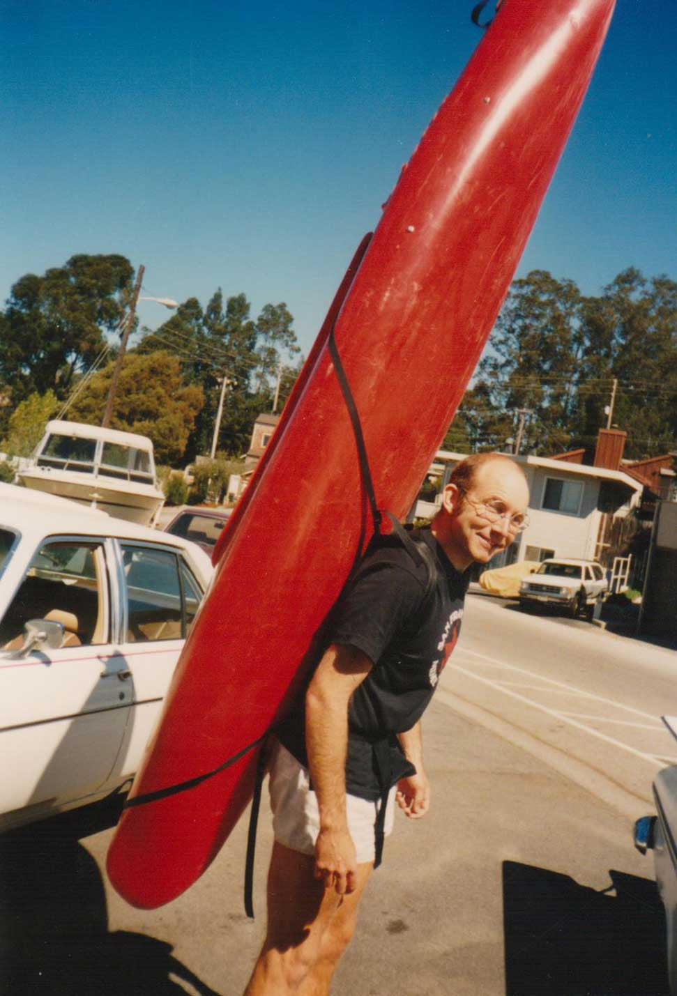 Tom designed and made a bag-less backpack that strapped to a kayak and allowed you to portage solo, late 1980s. He's using it to carry a red kayak!