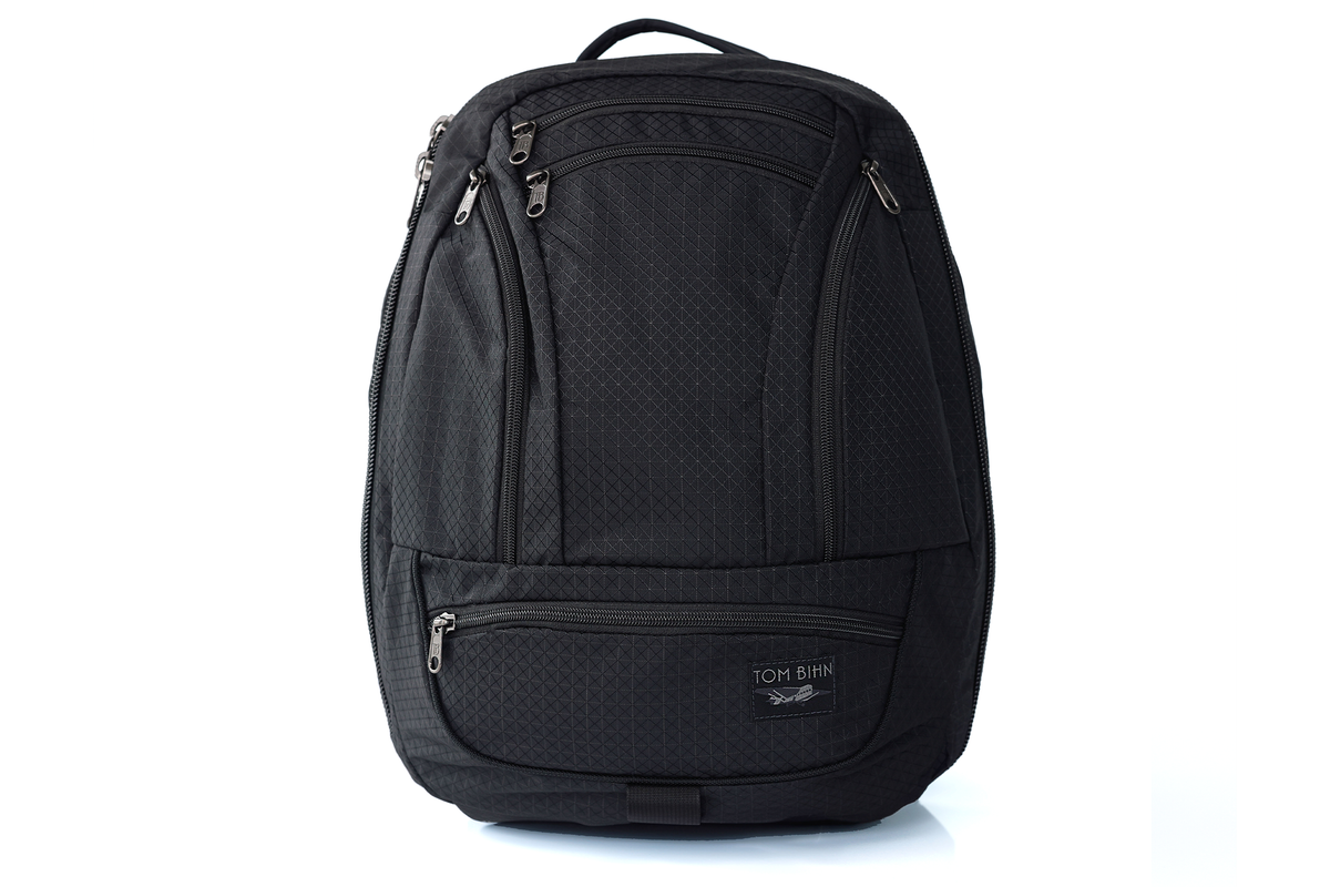 visible variant TB0122-BTND^^ A black TOM BIHN spectron backpack with multiple zippered compartments, shown on a clean white background.