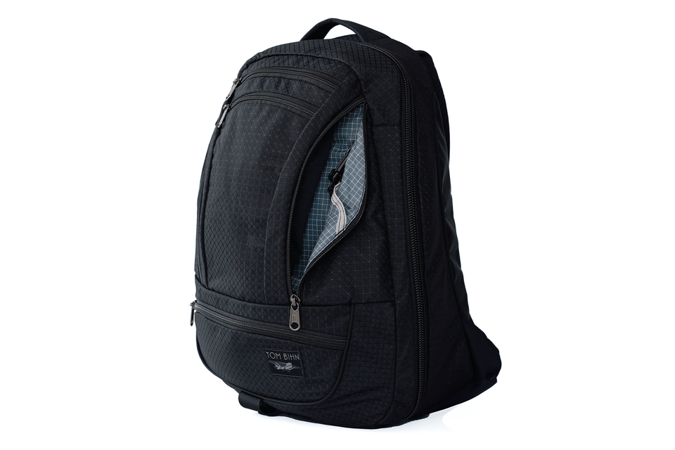 visible variant TB0122-BTND^^ A black backpack with a zippered front pocket and an open top compartment showing a gray interior, photographed on a white background.