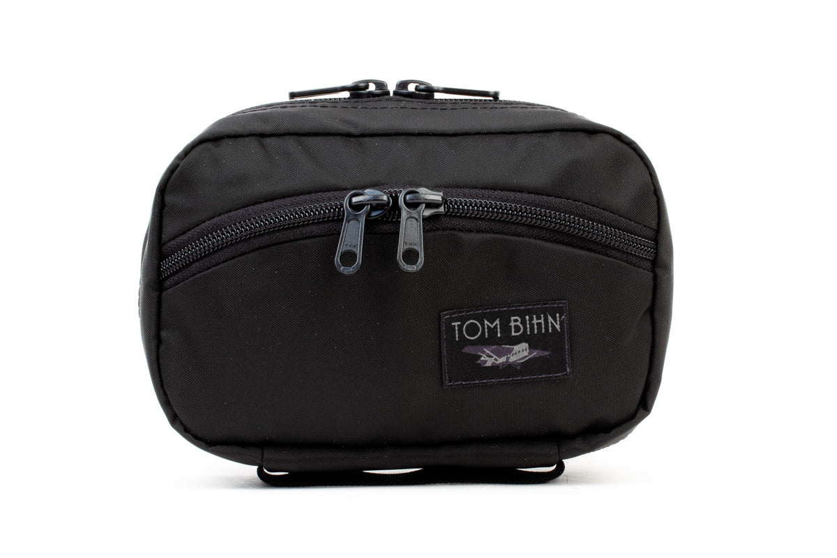 visible variant TB0418-BJ TB0418-BN^^The front of a Handy Little Thing #1 in Black 210 Ballistic showing the front zipper with two slider and logo at the bottom-right corner.