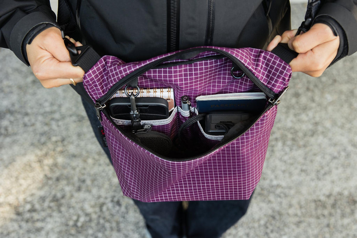 visible lifestyle^^Rogue Sacoche in Acai with a phone, camera, notepad, and passport inside.