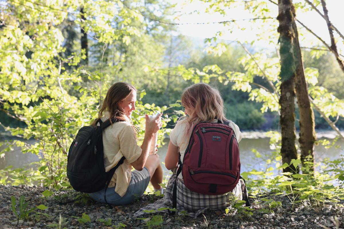 visible lifestyle^^Two friends wearing synapse 19, sitting in front of creek.