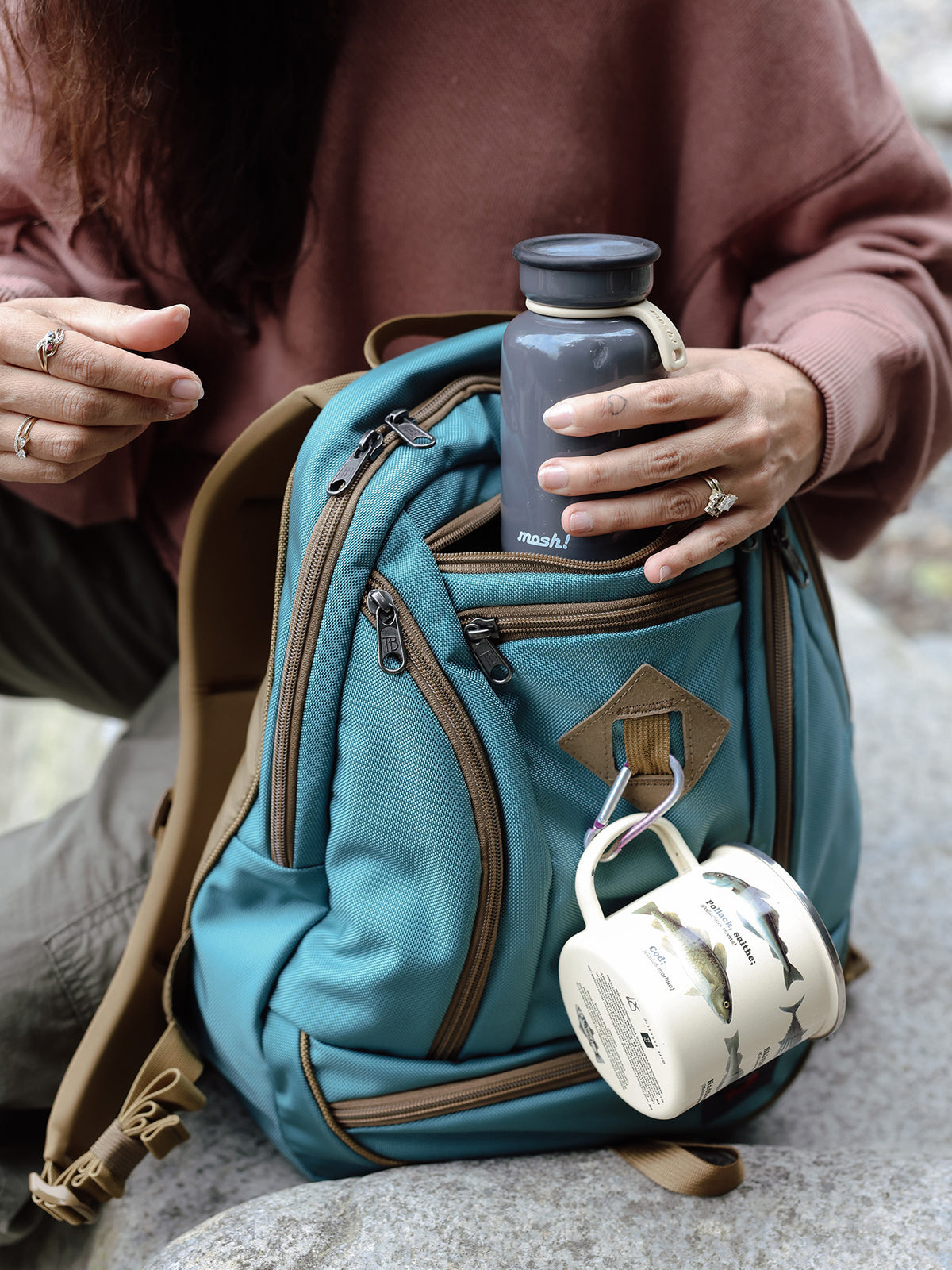 visible lifestyle^^A thermos being pulled from the center pocket of a GE Synapse 19 with a cup hooked on the front attachment point