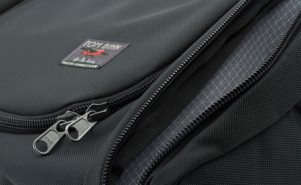 The label of the bag is offset to the right near the bottom of the main pocket's fabric lid. It features a red Farman Jaribu plane over a cityscape and the words "Portable Culture" embroidered near the bottom.