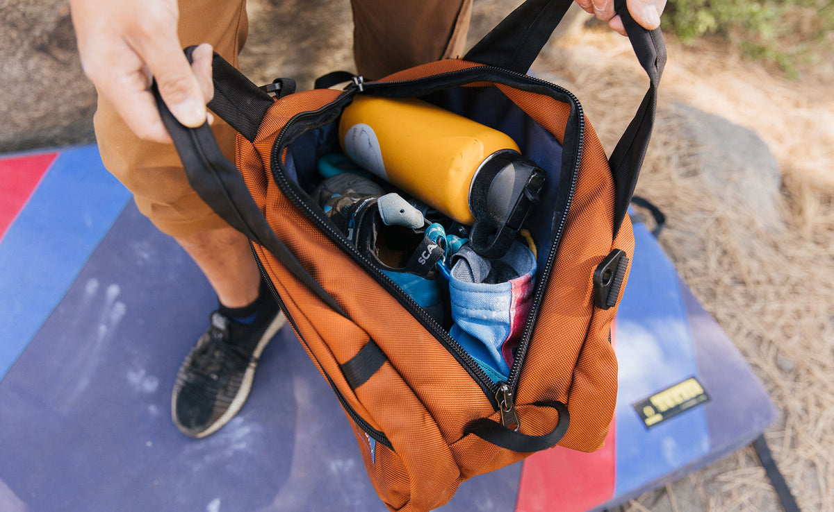 visible lifestyle^^A person holding the Old-School Carry All open: you can see inside of the main compartment and it's packed with a water bottle, chalk bag and other items.
