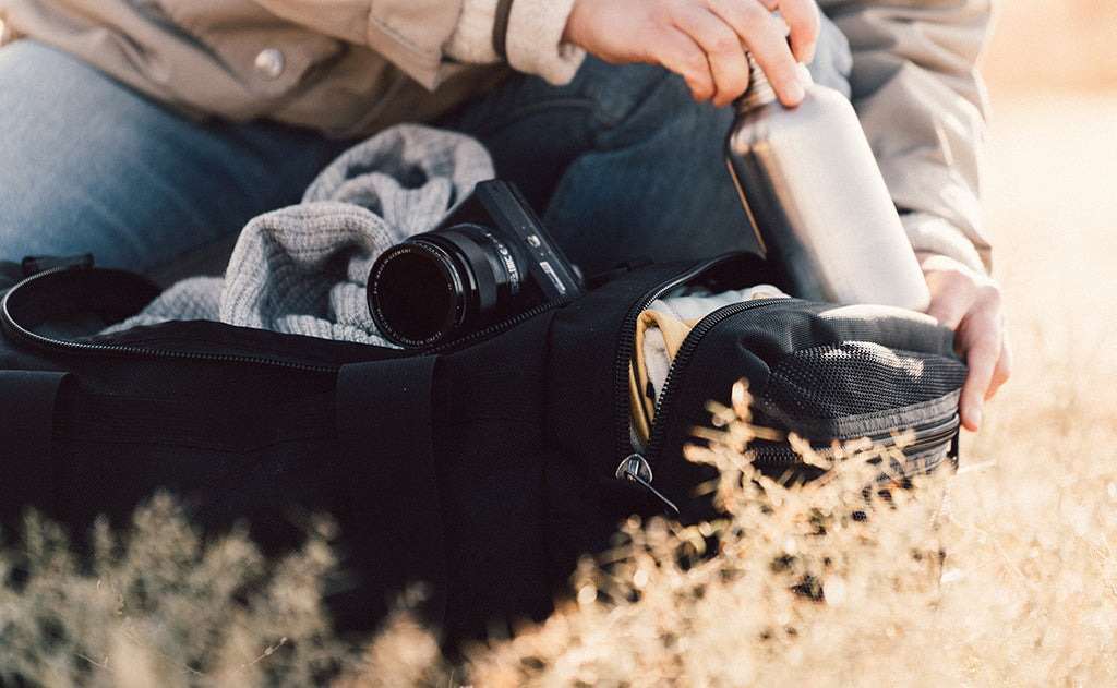 lifestyle visible^^A person placing a canteen in the Road Buddy Duffel 60's end pocket.