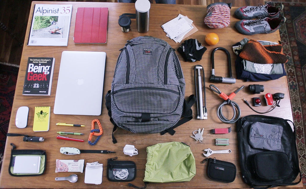 ^^A packing shot of the Synapse 25 with books, a tablet, biking gear, gym clothes, a water bottle, protein bars, and other various items.