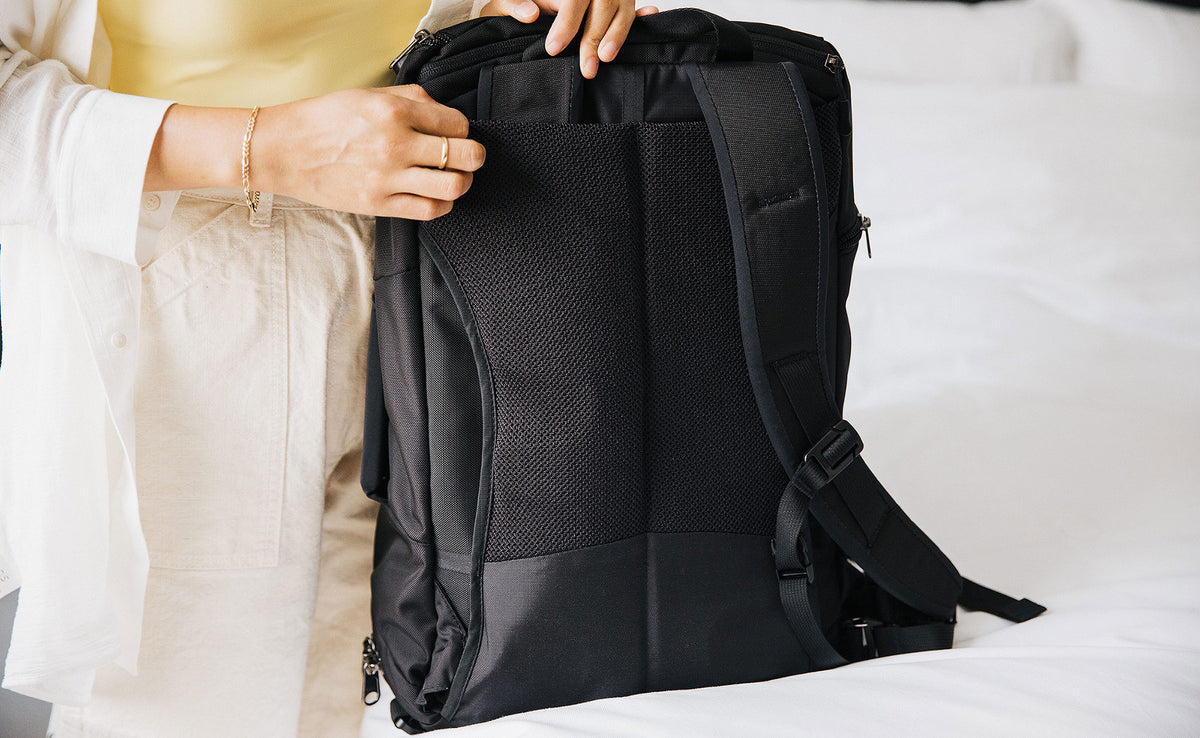 A person removing the shoulder straps of the Techonaut 30, showing the mesh of the back panel.