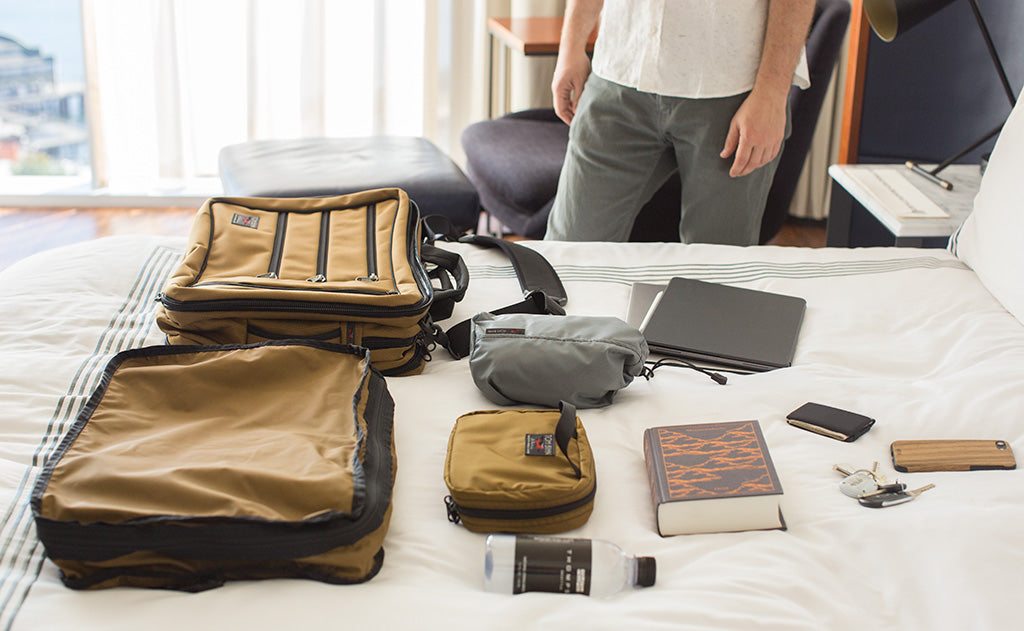 lifestyle visible^^A Tri-Star with a Tri-Star Packing Cube Backpack, Size 4 Travel Stuff Sack, Spiff Kit, laptop and cover, bottle of water, wallet, keys, phone, and hardback novel