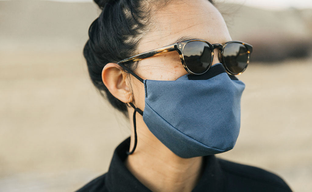 visible variant ME00012-LO^^Person standing outdoors in a grassy field wearing the V6 Mask in Pacific Blue. The person is wearing sunglasses.