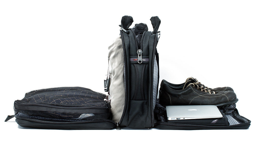 ^A Tri-Star with each of its main pockets filled with, from front to back, a pair of shoes and tablet in the front divided compartment, a packing cube in the middel pocket, and a packing cube and jacket in the rear main pocket.