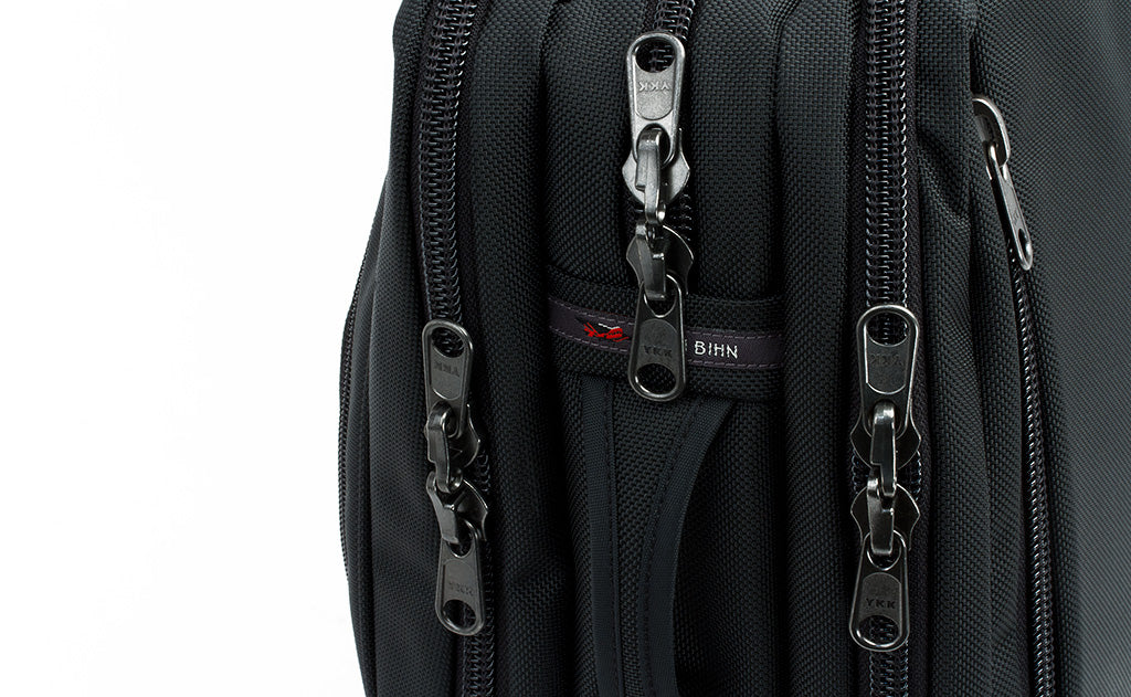 A close shot from a profile point of view of the three main pockets and their locking zippers as well as a side grab handle.