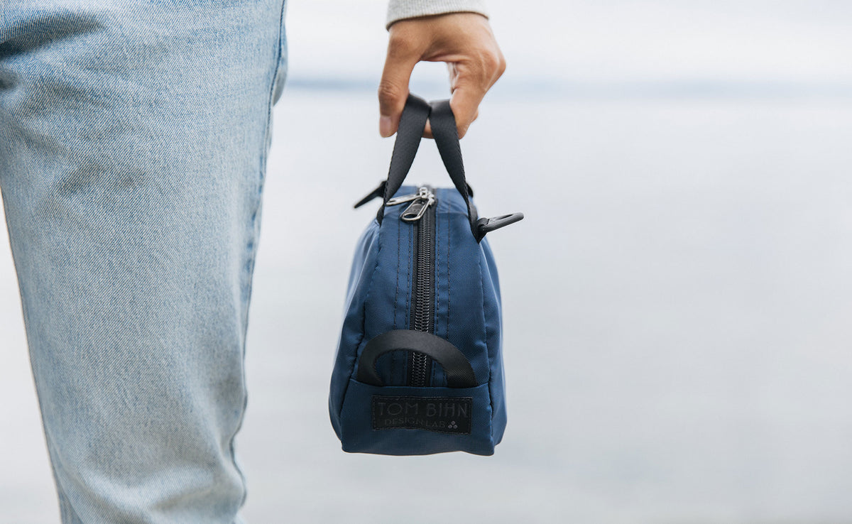 lifestyle visible^^ A person holding a Navy Parapack Grab Bag by it's grab handle showing the TOM BIHN Design Lab label. 