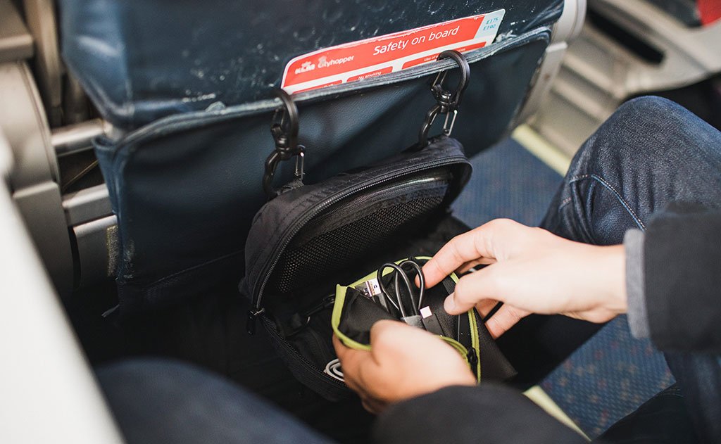 visible lifestyle ^^ A person retrieving a pouch from an HLT2 hung on the back of an airline seat pocket.