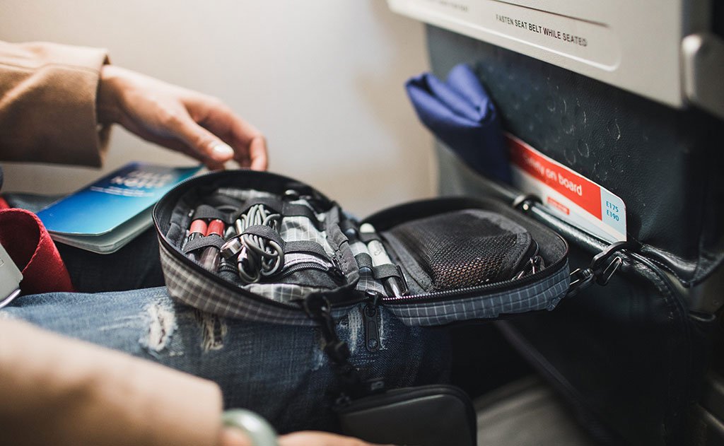 visible lifestyle ^^ A  person retrieving items from an HLT1 clipped to an airline seat pocket.