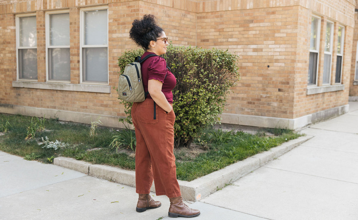 Person carrying the Paradigm backpack in Taiga 400d Halcyon. They're standing outdoors in front of a brick building.