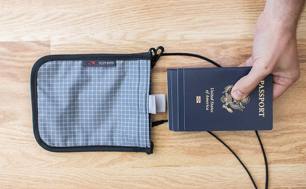 detail visible^^A person inserting 4 US Passports into a Passport Pouch.