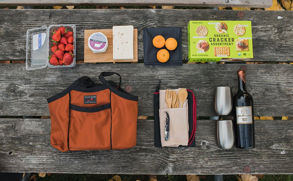  lifestyle visible ^^ A possible packing list for the Pick Up Truck, including a wine bottle, two glasses, a cutlery set, a box of crackers, fruit, and cheese.
