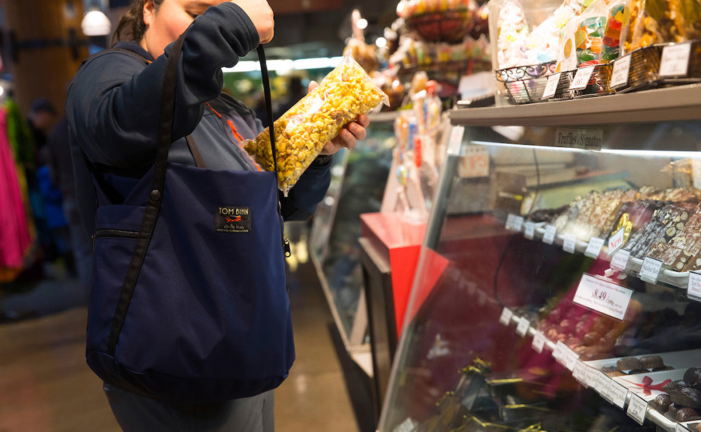 ^^A person putting a sealed bag of popped popcorn in the main compartment of the Pop Tote.
