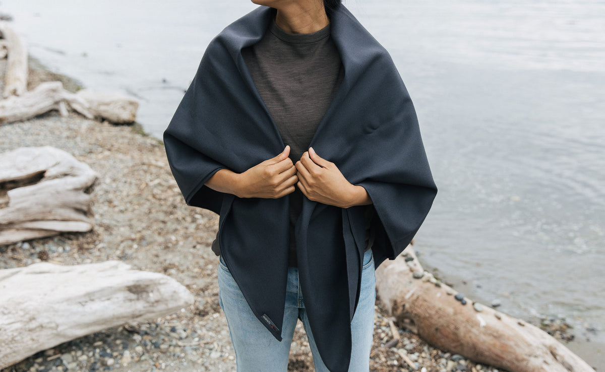 lifestyle visible^^ A Large Shepherd's Wool Utility Cloth in Matter Grey being worn as a shawl by a person at the beach.
