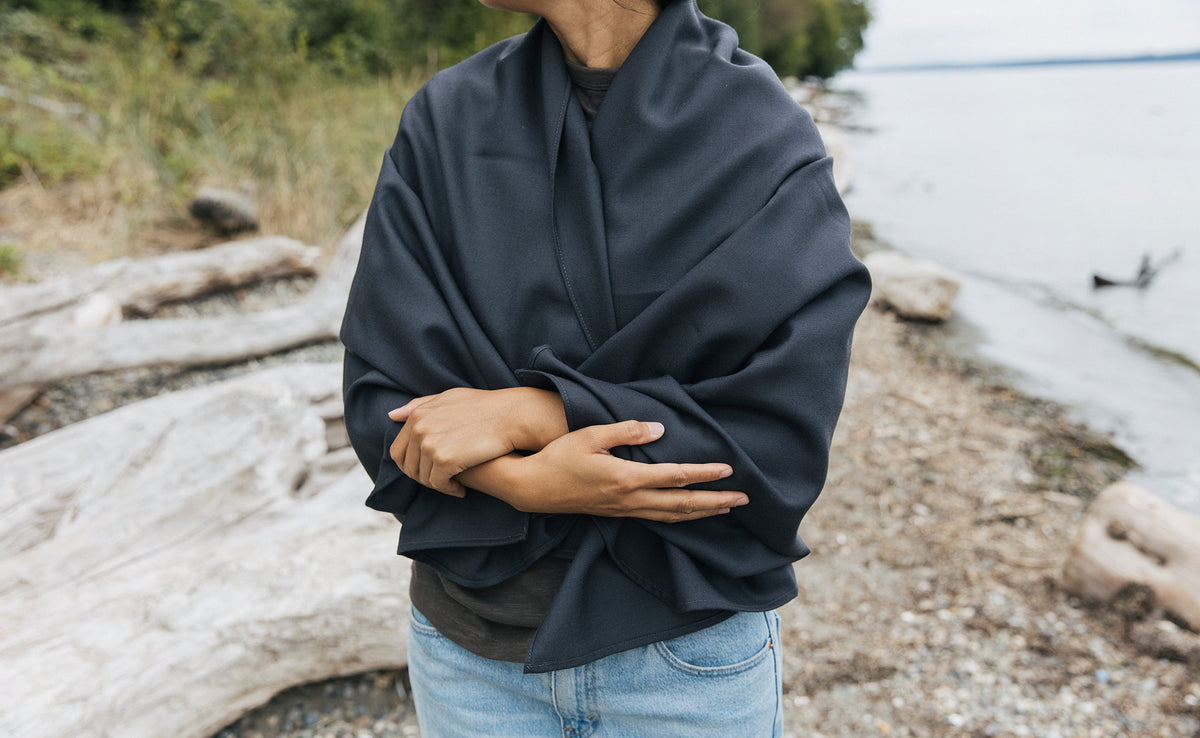 lifestyle visible^^ A Large Shepherd's Wool Utility Cloth in Matter Grey wrapped around a person's shoulders and torso at the beach. 