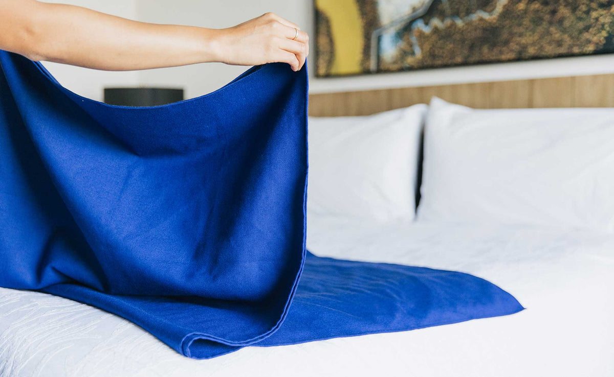 lifestyle visible^^ A Large Shepherd's Wool Utility Cloth in Neela Blue being folded on a hotel bed.